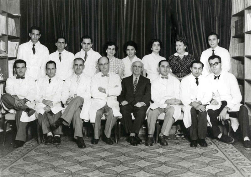 Fig 5. Parte del personal de la Fundación Luis Roche. De izquierda a derecha, sentados: Jorge Vera, Mario Calcinay, Miguel Layrisse, Marcel Roche, Luis Roche, Francisco de Venanzi, Gabriel Chuchani y Luis M. Carbonell; de pie: Abraham Levy, Andrés Gerardi, José Forero, Leocadia Escalona, María Enriqueta Tejera, Gloria Villegas, Slavka Hitrovo y Francisco Peña.