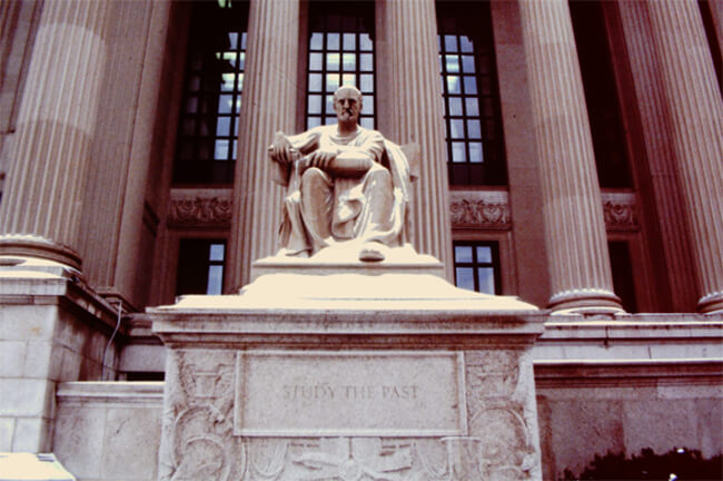 1C Figura 1. Los Archivos Nacionales (National Archives): 1A. Frontispicio De Los Archivos Nacionales (National Archives). 1b, Estatua Lateral Izquierda. El escultor fue Robert I. Aitken (1878-1949). La estatua de la dama “Futuro”, con el libro abierto, por ser escrito, y citando a Shakespeare (La Tempestad), reza: Lo que es pasado es prólogo (What is Past is Prologue). 1C. Estatua Lateral Derecha. La estatua del hombre “Pasado”, con el libro cerrado y ya escrito, cita a Confucio: Estudia el pasado (Study the Past).